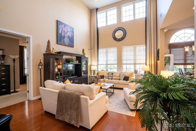 living room featuring a towering ceiling, a healthy amount of sunlight, an inviting chandelier, and dark wood-type flooring