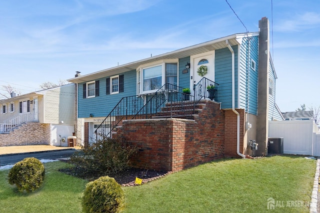 ranch-style home featuring a front yard, cooling unit, fence, a chimney, and brick siding