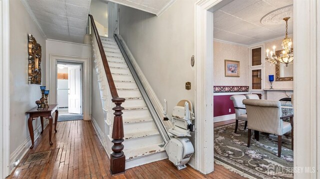 staircase featuring hardwood / wood-style floors, ornamental molding, and an inviting chandelier