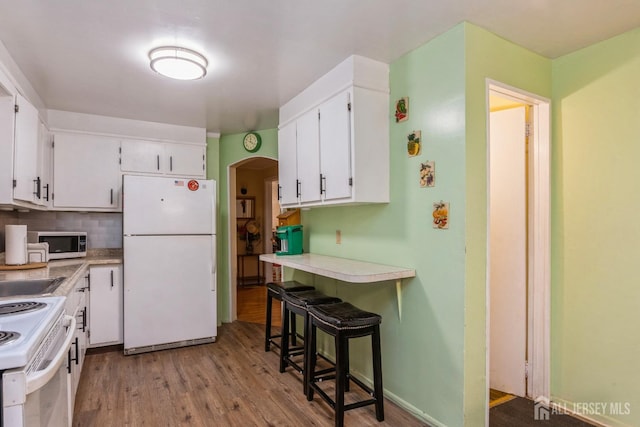 kitchen featuring a kitchen breakfast bar, backsplash, white appliances, white cabinets, and light hardwood / wood-style floors