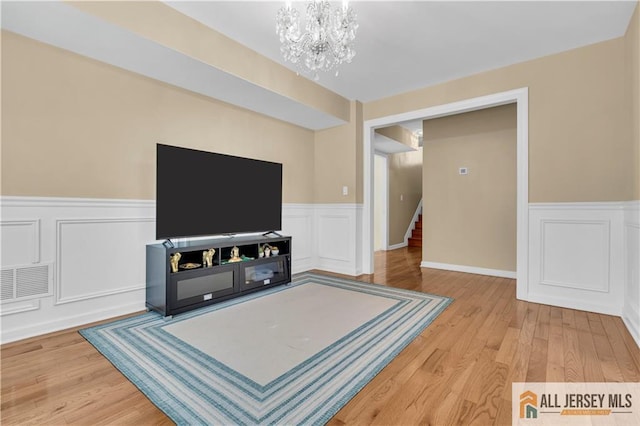 living room with a chandelier, wainscoting, stairs, wood finished floors, and a decorative wall