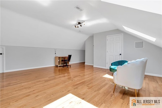 sitting room featuring a skylight, lofted ceiling, light wood-type flooring, baseboards, and rail lighting