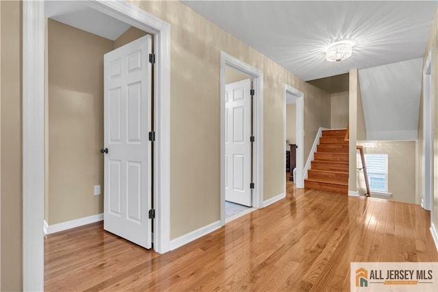 hallway featuring light wood finished floors, stairs, and baseboards