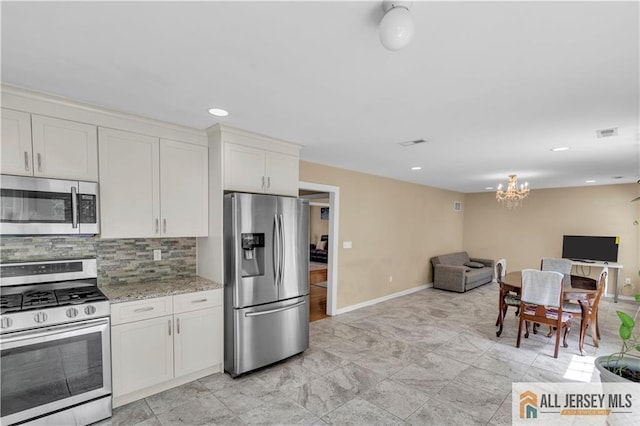 kitchen featuring appliances with stainless steel finishes, a chandelier, baseboards, open floor plan, and tasteful backsplash