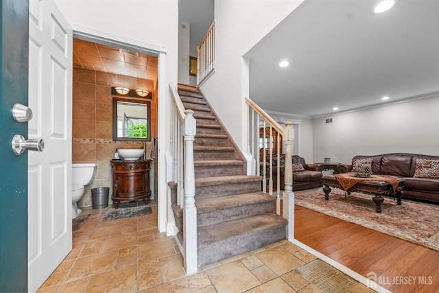 stairway featuring hardwood / wood-style floors, tile walls, and ornamental molding