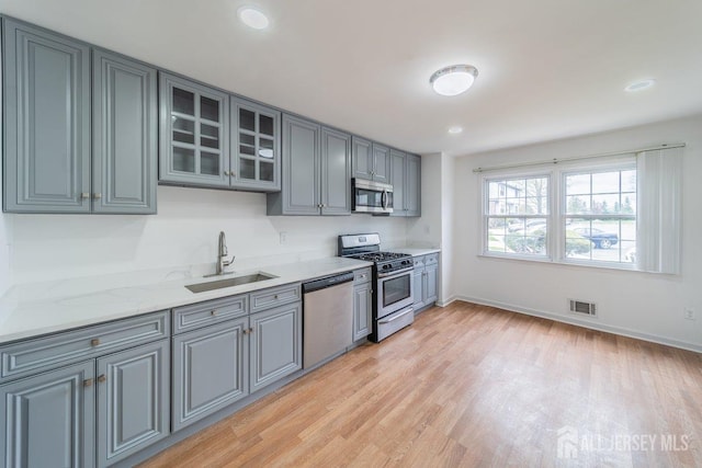 kitchen with appliances with stainless steel finishes, a sink, gray cabinetry, light wood-style flooring, and recessed lighting