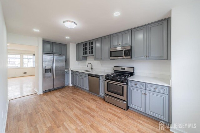 kitchen featuring appliances with stainless steel finishes, gray cabinets, a sink, light countertops, and light wood-style floors