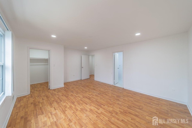 unfurnished bedroom with light wood-type flooring, recessed lighting, a walk in closet, baseboards, and a closet