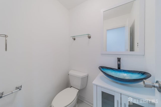 half bathroom with vanity, toilet, and baseboards