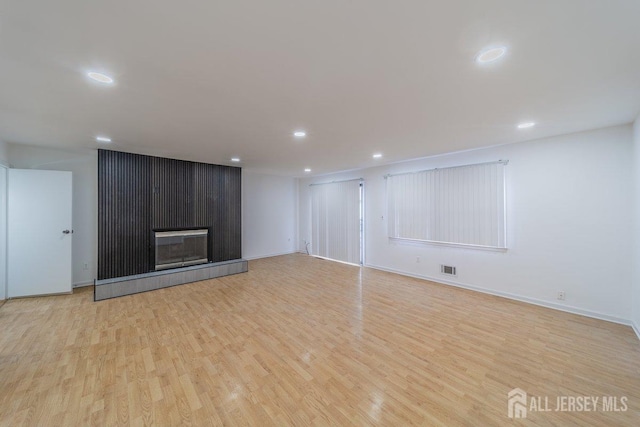 unfurnished living room with wood finished floors, recessed lighting, baseboards, and a tiled fireplace