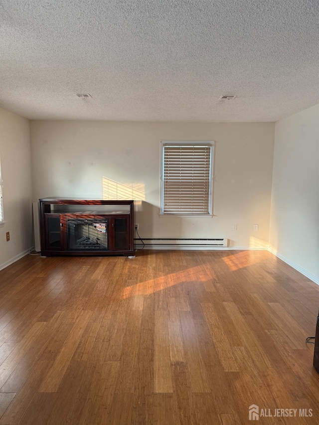 469-O New Haven Way, Monroe, NJ 08831 - unfurnished living room with a baseboard radiator, wood finished floors, a textured ceiling, and baseboards