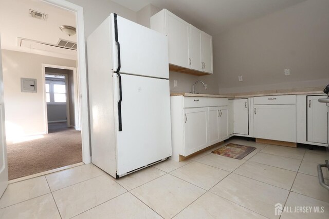 kitchen featuring white refrigerator, sink, light tile patterned floors, and white cabinets