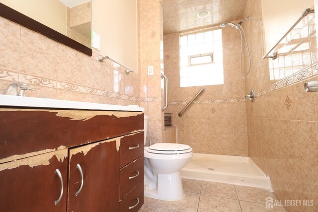 bathroom featuring tile walls, vanity, a tile shower, tile patterned floors, and toilet