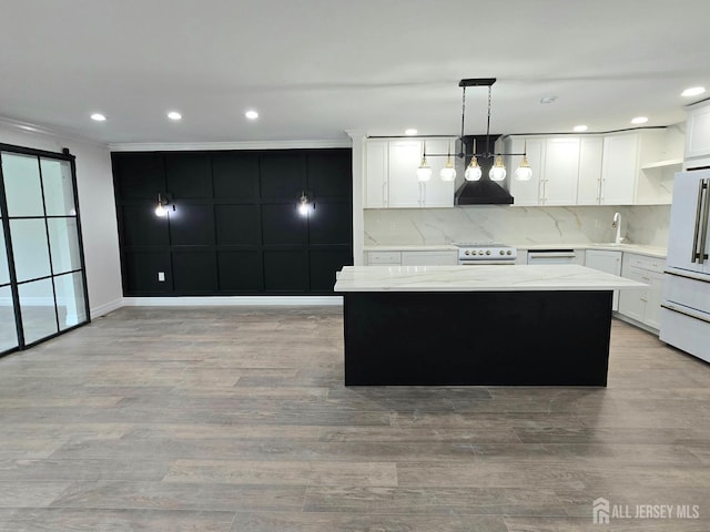 kitchen featuring freestanding refrigerator, a center island, a sink, light wood finished floors, and decorative light fixtures