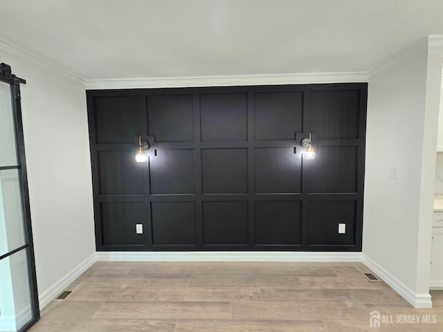 interior space featuring baseboards, ornamental molding, a barn door, and light wood-type flooring