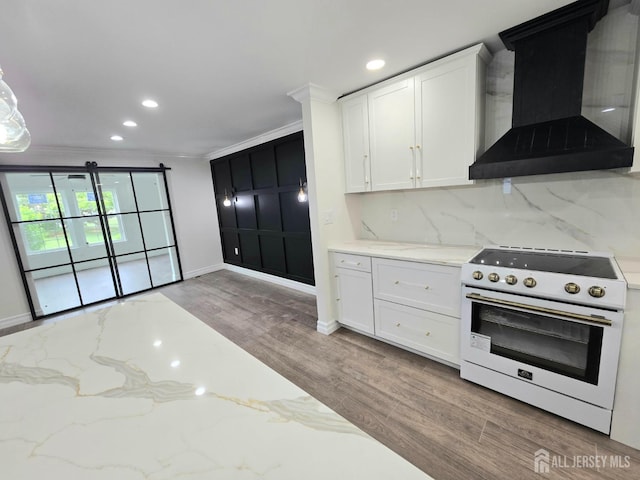 kitchen with wall chimney range hood, white range with electric cooktop, white cabinets, and wood finished floors