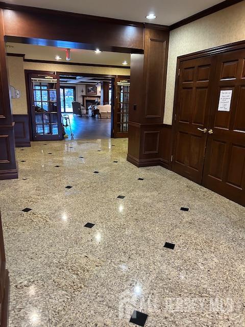 hall with ornamental molding, wainscoting, granite finish floor, and a decorative wall