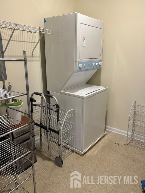 laundry area featuring stacked washer and dryer, light colored carpet, laundry area, and baseboards