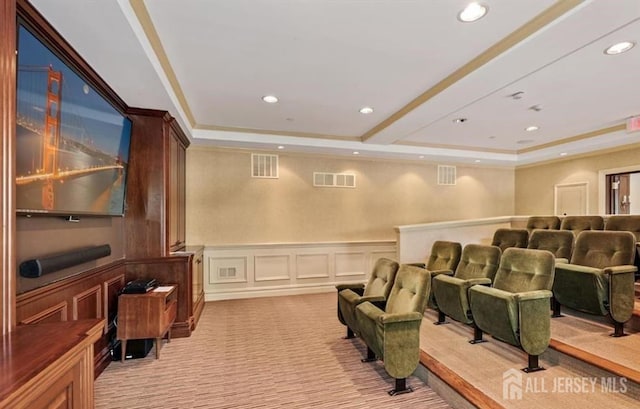 cinema room with a tray ceiling, a wainscoted wall, visible vents, and light carpet