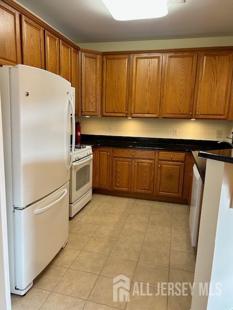 kitchen with dark countertops, light tile patterned flooring, brown cabinets, and white appliances
