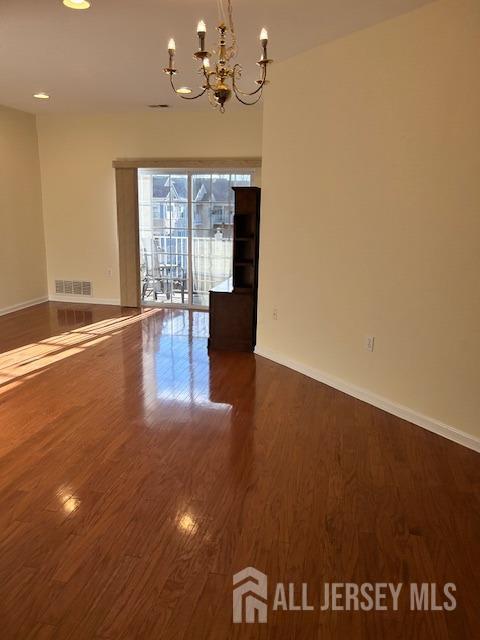 empty room with an inviting chandelier, baseboards, wood finished floors, and visible vents