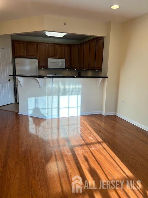 kitchen featuring white appliances, baseboards, dark countertops, a kitchen breakfast bar, and dark wood-style flooring