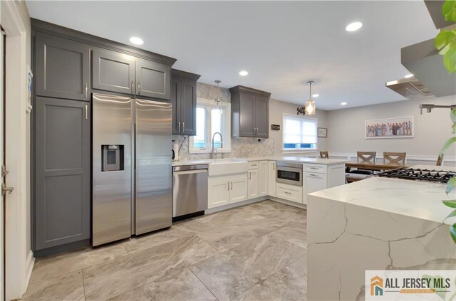 kitchen featuring sink, appliances with stainless steel finishes, white cabinetry, hanging light fixtures, and light stone counters