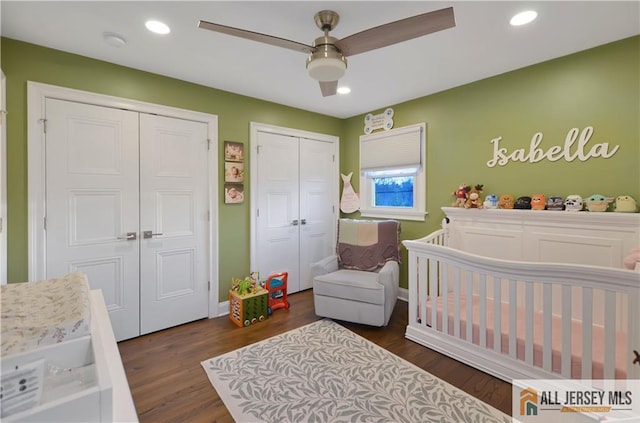 bedroom with multiple closets, a nursery area, dark wood-type flooring, and ceiling fan