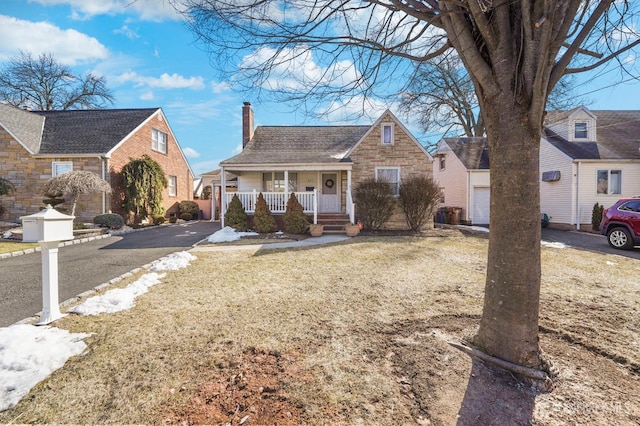 view of front facade featuring a front yard, a shingled roof, a porch, aphalt driveway, and a chimney