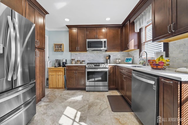 kitchen featuring tasteful backsplash, light countertops, crown molding, appliances with stainless steel finishes, and a sink