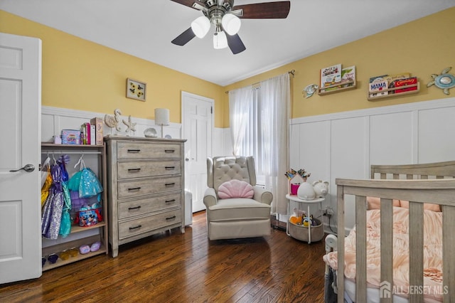 bedroom with a decorative wall, ceiling fan, dark wood-style floors, and a wainscoted wall