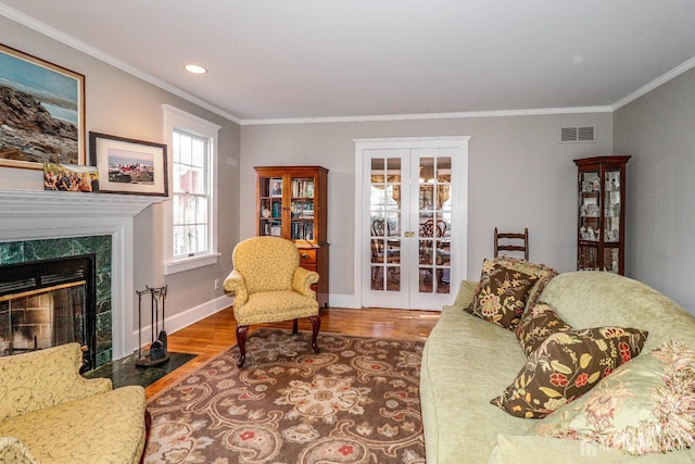 living room featuring wood finished floors, visible vents, a premium fireplace, ornamental molding, and french doors