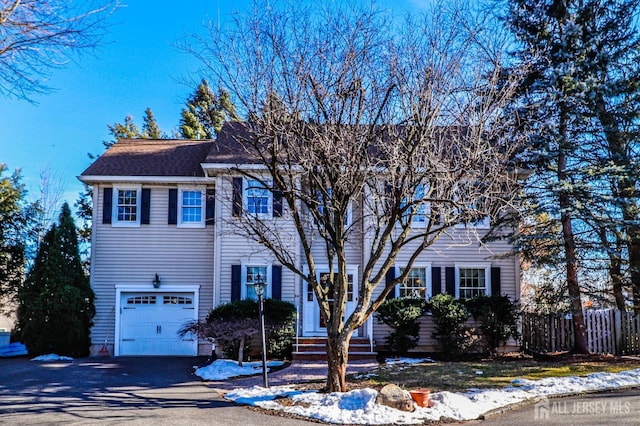 colonial house with aphalt driveway, an attached garage, entry steps, and fence