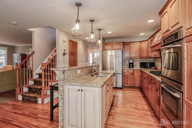 kitchen with a breakfast bar area, stainless steel appliances, a sink, light wood-type flooring, and a wealth of natural light