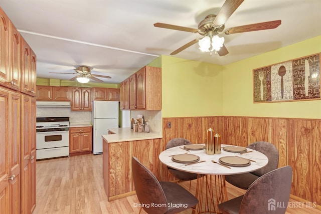 kitchen featuring white appliances, light hardwood / wood-style flooring, ceiling fan, backsplash, and wood walls