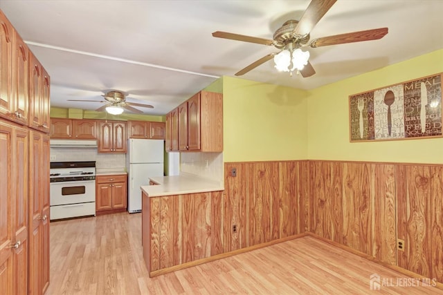 kitchen with tasteful backsplash, white appliances, light wood-type flooring, wooden walls, and ceiling fan