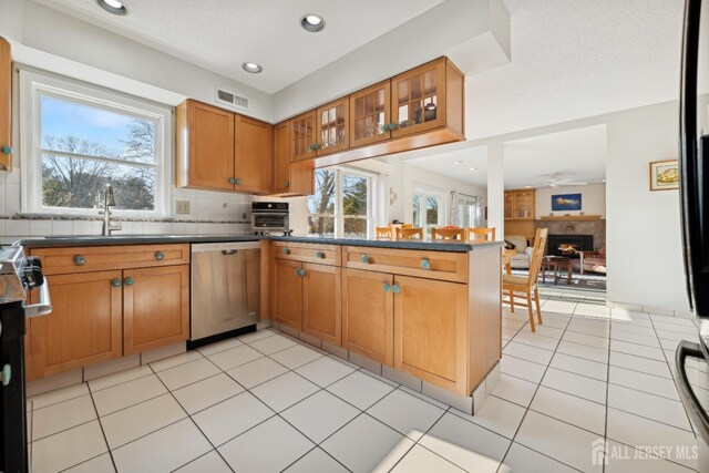 kitchen with sink, tasteful backsplash, light tile patterned floors, stainless steel dishwasher, and kitchen peninsula