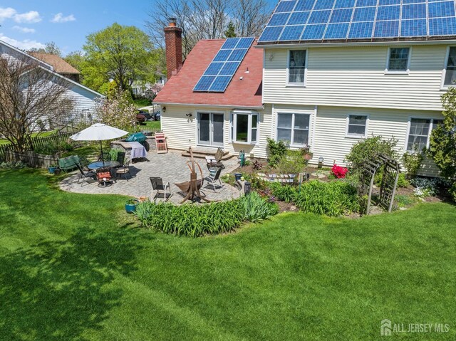 rear view of property featuring a yard, a patio area, and solar panels