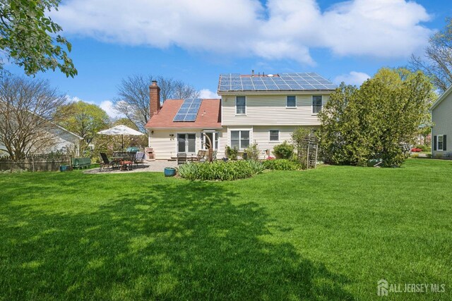 rear view of property with a lawn, a patio area, and solar panels