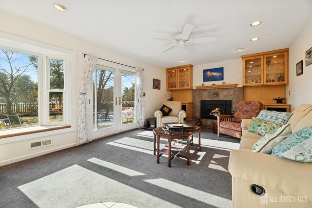 living room with dark colored carpet, ceiling fan, a fireplace, and french doors