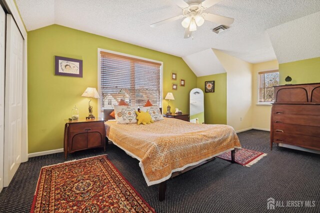 bedroom featuring ceiling fan, vaulted ceiling, a textured ceiling, and dark colored carpet