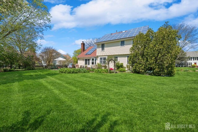 rear view of house featuring a lawn and solar panels