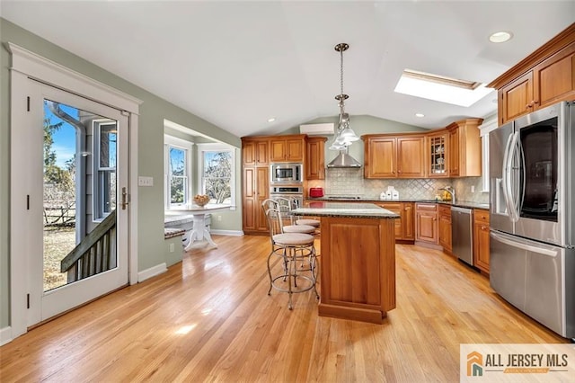 kitchen with vaulted ceiling with skylight, a kitchen bar, stainless steel appliances, brown cabinets, and decorative backsplash