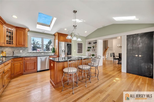 kitchen with vaulted ceiling with skylight, a kitchen breakfast bar, brown cabinets, stainless steel appliances, and a kitchen island
