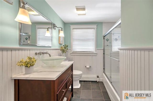 full bath featuring a baseboard heating unit, tile patterned flooring, plenty of natural light, and a wainscoted wall