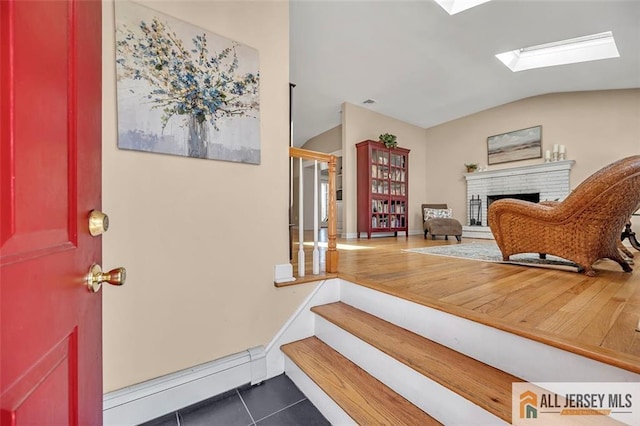 entryway featuring vaulted ceiling with skylight, a brick fireplace, dark tile patterned floors, stairway, and a baseboard heating unit