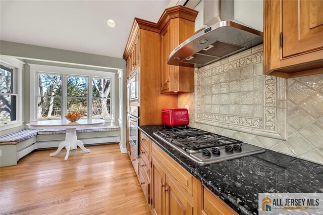 kitchen with brown cabinetry, light wood-type flooring, appliances with stainless steel finishes, and wall chimney exhaust hood