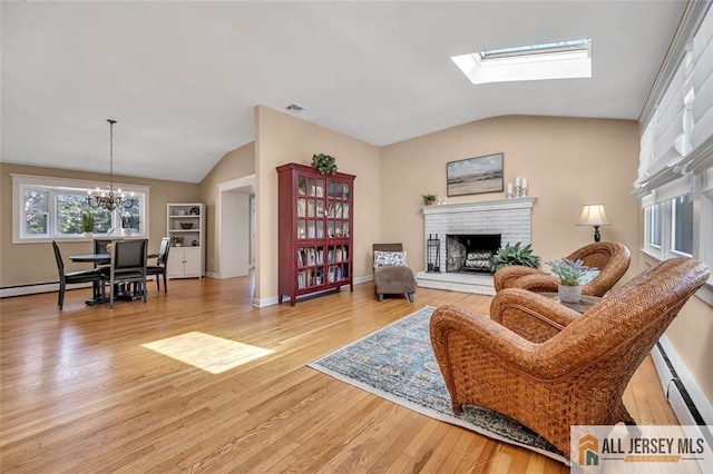 living room featuring a fireplace, vaulted ceiling with skylight, light wood-style floors, and an inviting chandelier