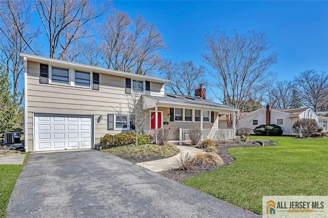 split level home with driveway, a front lawn, covered porch, a garage, and a chimney