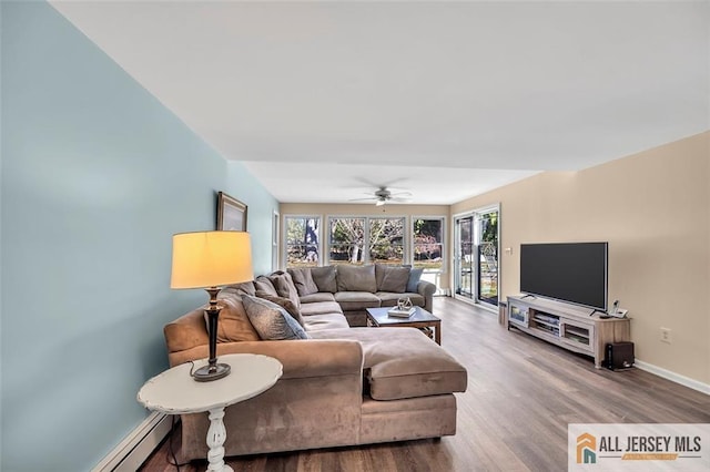 living area with baseboard heating, wood finished floors, ceiling fan, and baseboards